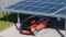 Imaginea prezintă un carport cu module fotovoltaice pe acoperiș și o mașină electrică în curs de încărcare.